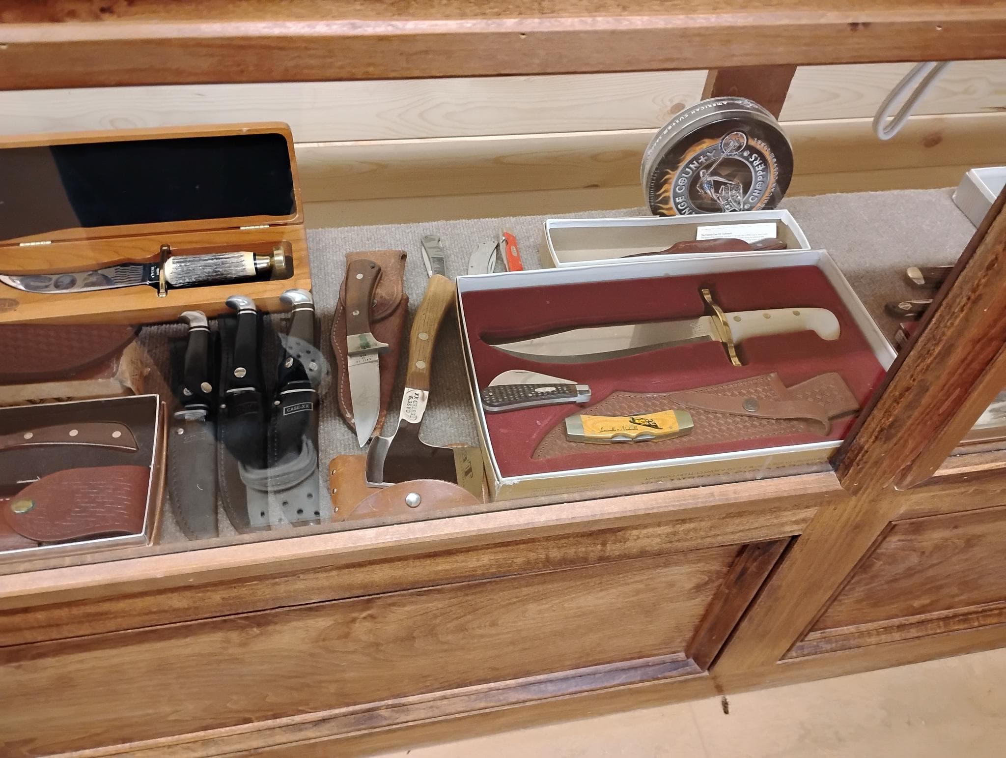 Lower display shelf — stag-handle fixed blade, stack of black-handled utility knives, Bowie set with Case sheath.